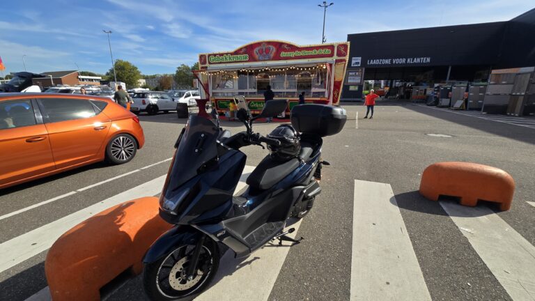 Zwarte scooter geparkeerd op een parkeerterrein met een gebakkraam op de achtergrond